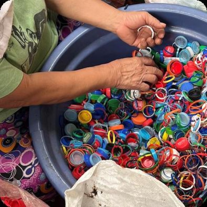 Two hands sorting a basin brimming with colourful plastic bottle caps into a sack for weighing